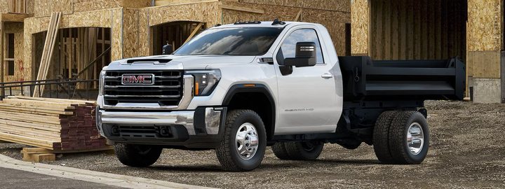 GMC Sierra 3500HD Chassis Cab in white with a black dump body, parked at a timber-framed construction site